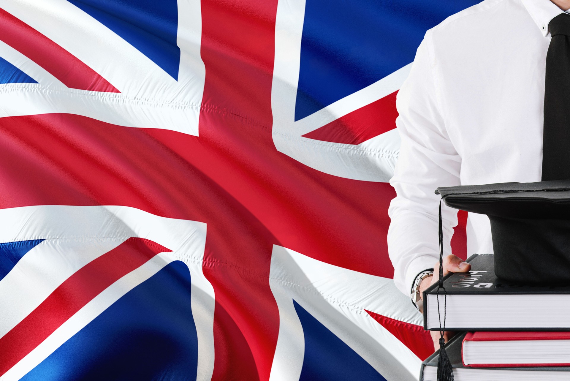Concept d'éducation étudiante britannique réussi. Tenue de livres et casquette de graduation sur fond de drapeau du Royaume-Uni.