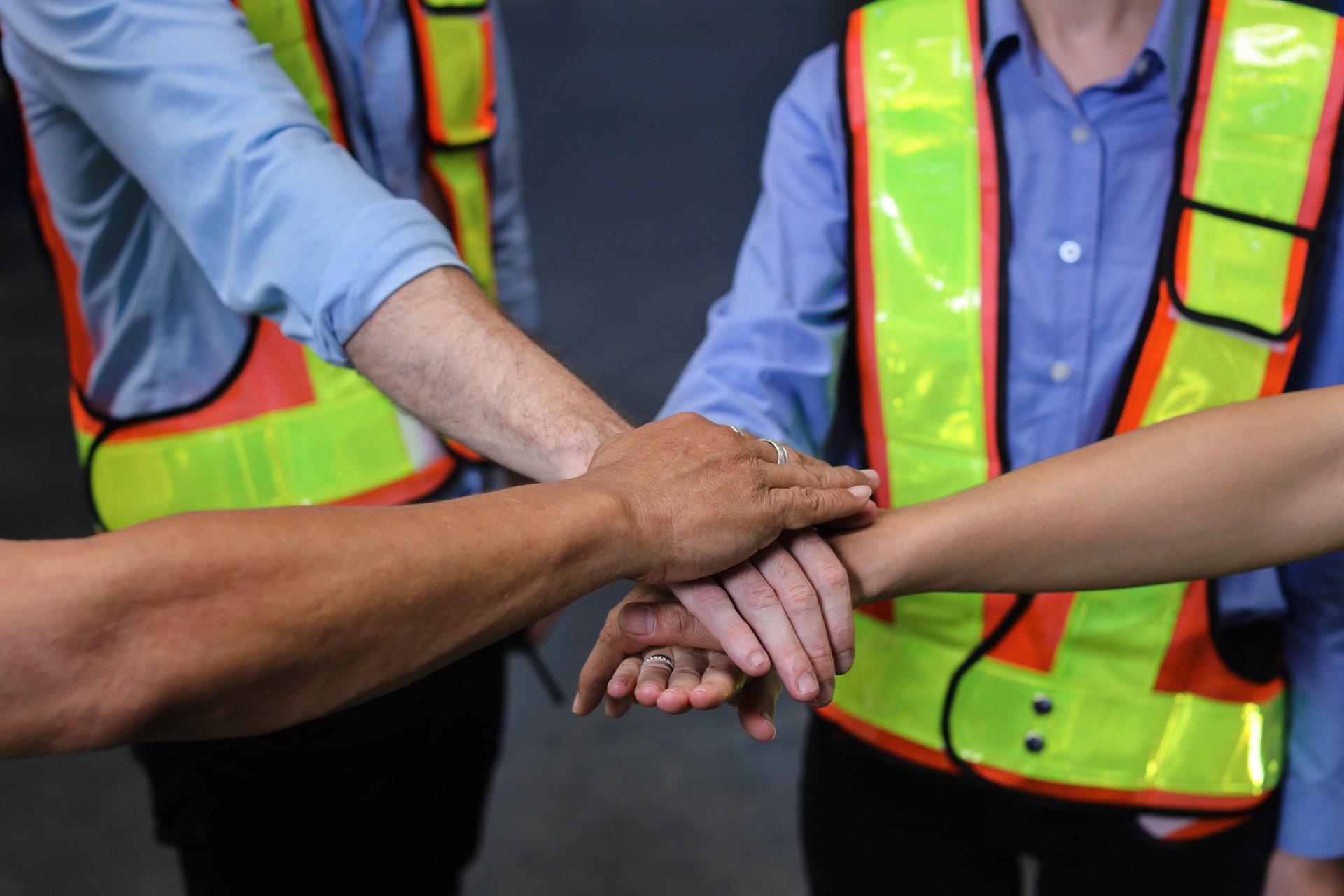 Un groupe d’ingénieurs ou de travailleurs en combinaison de protection avec casque de sécurité debout et les mains empilées célèbrent ensemble ou achevé un engagement réussi dans une usine ou un entrepôt de fabrication de l’industrie lourde